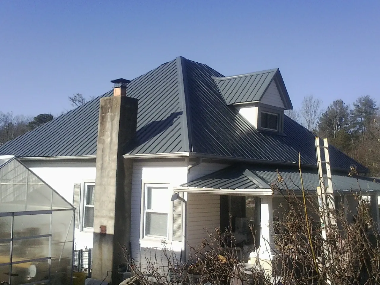 Dark blue standing seam metal roof on a white farmhouse with dormer — Slate & Tile Roof Repair by Roofing Brothers in Grace