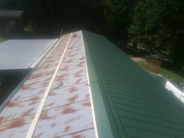 Old rusted panels beside newly installed green metal roofing — Wind Damage Roof Repair by Roofing Brothers in Grace