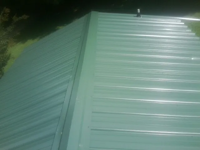 New green metal panels meeting at the ridge of a roof — Flat Roof Repair work by our crew in Grace
