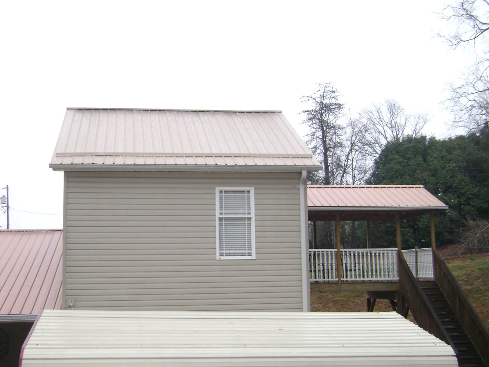 Tan metal roofs on a two story addition and attached porch, from a Roof Replacement job in Grace